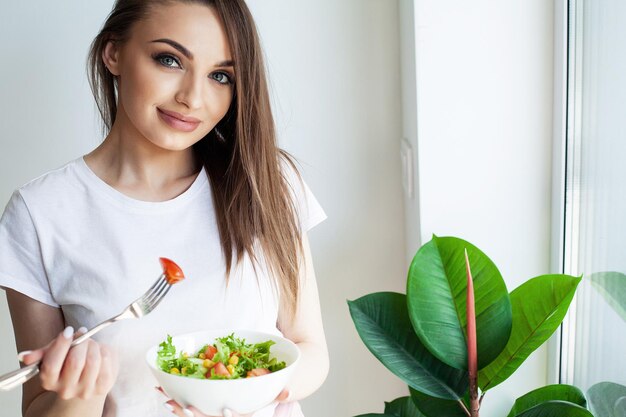 Gesunde Lebensstilfrau, die Salat isst und in der leichten Küche glücklich lächelt