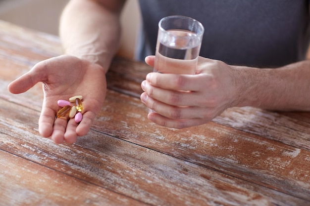 Gesunde Lebensweise, Medizin, Nahrungsergänzungsmittel und Menschen Konzept - Nahaufnahme von männlichen Händen halten Pillen mit Lebertran Kapseln und Wasser Glas