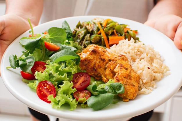 Gesunde Mahlzeit mit gegrilltem Hühnerreissalat und Gemüse, serviert von einer Frau