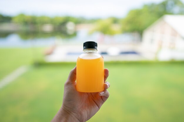 Gesunde Orangensaftentgiftung. Nahaufnahme der frischen orange Flasche in der Hand und im grünen Naturhintergrund.