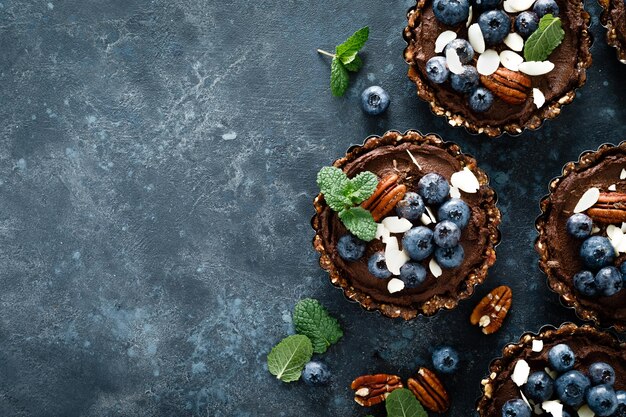 Gesunde rohe vegane Dessert-Dattel-Törtchen mit Schokoladen-Cashew-Creme, dekoriert mit Mandel-Pekannuss-Nüssen und frischer Blaubeere