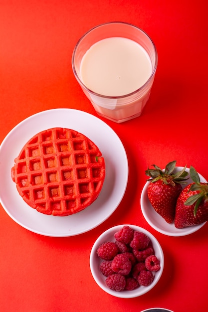 Gesunde rote Waffeln mit Fruchthonig und Milch auf rotem Hintergrund mit verschiedenen Winkeln