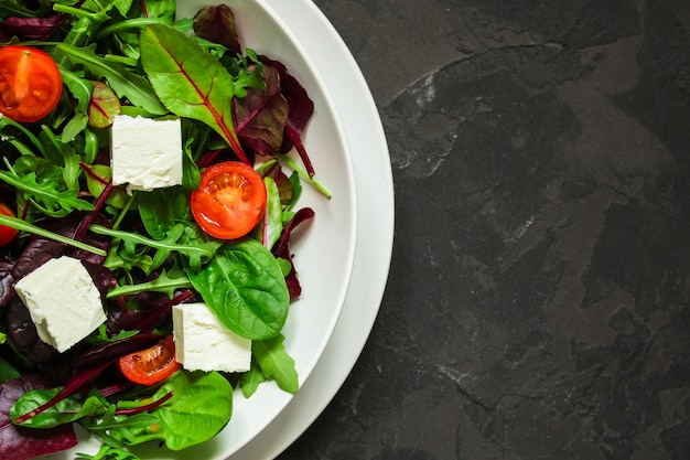 Gesunde Salatblätter in einer weißen Platte und in einem Käse (Mischungsgrüns). Essen Hintergrund