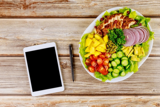 Gesunde Salate mit Tablette und Stift auf Holztisch