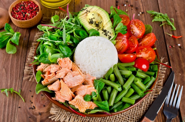 Gesunde Salatschüssel mit Lachs, Reis, Tomaten, Avocado, Mischsalat, grünen Bohnen