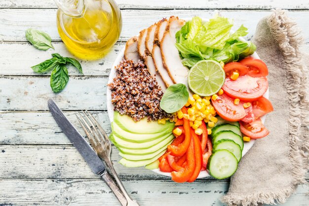 Gesunde Salatschüssel mit Quinoa, Tomatentruthahn, Avocado, Paprika, Mais, Limette und gemischtem Grün, Draufsicht. Gesunde Lebensmittelkonzeption. Superfood-Mahlzeit.