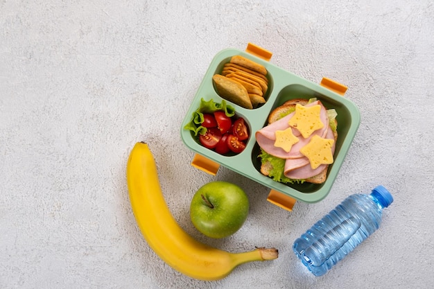 Gesunde Schulbrotdose mit Sandwich und Salat auf dem Tisch Bananenapfel und eine Flasche Wasser Zurück zur Schule