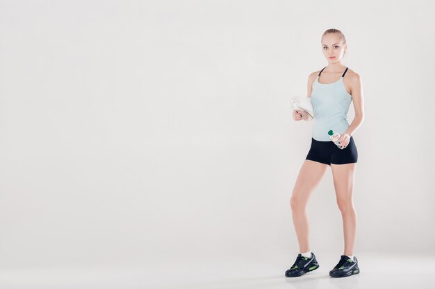 Gesunde Sportfrau in Fitnesskleidung mit Gymnastiktuch und Wasserflasche. Sanftes Licht