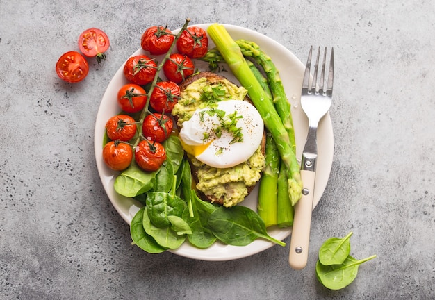 Gesunde vegetarische Mahlzeit Platte. Toast, Avocado, pochiertes Ei, Spargel, gebackene Tomaten, Spinat.