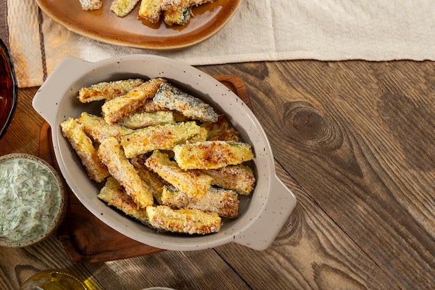 Gesunde Zucchini-Frites mit Joghurt- und Kräutersauce auf einem Holztisch