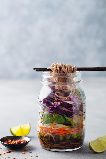 Gesunder asiatischer Salat mit Nudeln, Gemüse, Huhn und Tofu in Gläsern. Grauer Hintergrund. Kopierraum