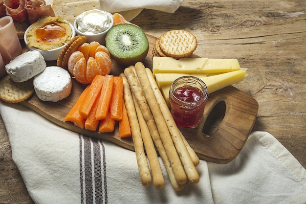 Gesunder Brunch Tisch zum Mitnehmen mit Schinken, Erdbeeren; Kiwi; Brot; Kekse; Käse, Karotten, Mandarinen, Hummus.