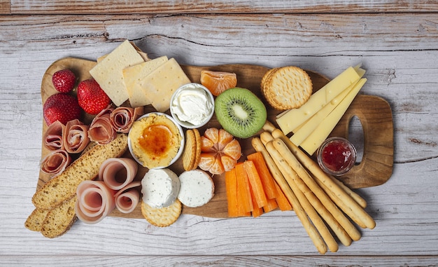 Gesunder Brunch Tisch zum Mitnehmen mit Schinken, Erdbeeren; Kiwi; Brot; Kekse; Käse, Karotten, Mandarinen, Hummus.