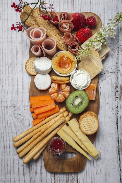 Gesunder Brunch Tisch zum Mitnehmen mit Schinken, Erdbeeren; Kiwi; Brot; Kekse; Käse, Karotten, Mandarinen, Hummus.