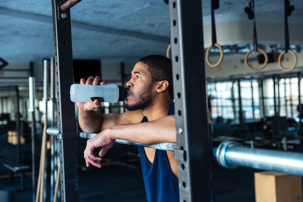 Gesunder Fitness-Mann trinkt Wasser beim Ausruhen im Fitnessstudio