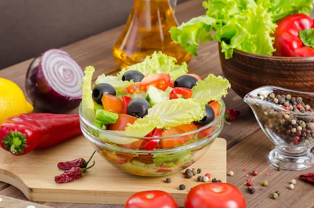 Gesunder Frischgemüsesalat mit Tomaten, Gurken und Oliven in einem Teller auf dunklem Holzhintergrund