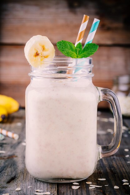 Gesunder Frühstücks-Bananen-Smoothie mit Haferflocken im Glasmaurerglas auf Holzhintergrund