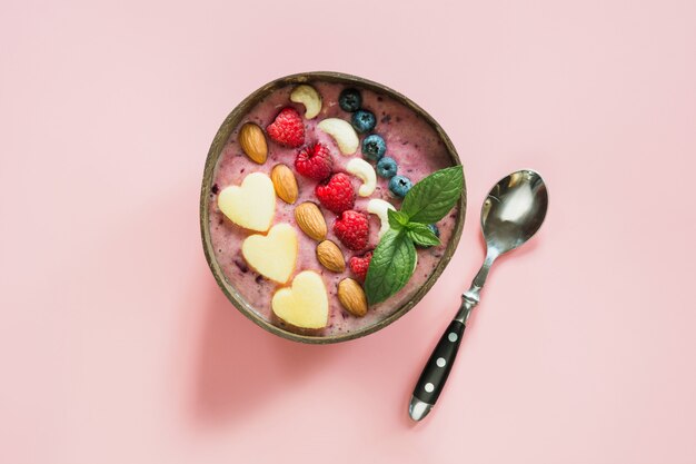 Gesunder Frühstücksbananen- und Blaubeerensmoothie verziert mit Früchten in der Kokosnussschüssel auf Rosa.