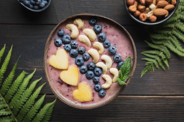 Gesunder Frühstücksbananen- und Blaubeerensmoothie verziert mit Früchten in der Kokosnussschüssel.