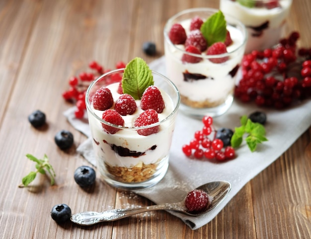 Gesunder Frühstücksjoghurt mit frischen Beeren und Müsli, serviert im Glasgefäß auf Holzhintergrund