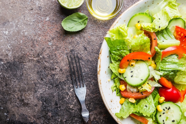 Gesunder Gemüsesalat aus frischen Tomaten, Gurken, Salat und Mais auf Teller, Draufsicht. Diät-Menü.