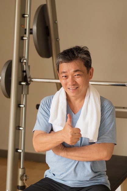 Gesunder, glücklicher älterer Mann, der im Fitnessstudio trainiert und Daumen-oben-Geste aufgibt