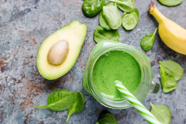 Gesunder grüner Smoothie mit Spinat, Avocado, Banane und Chiasamen in Gläsern auf grauem Steinhintergrund, Draufsicht.