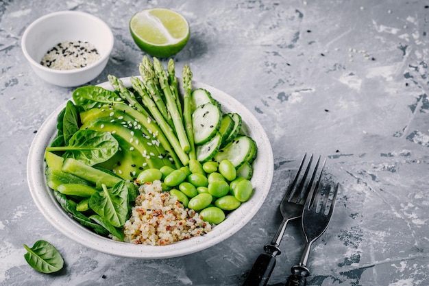 Gesunder grüner vegetarischer Buddha-Bowl-Salat mit frischem Gemüse und Quinoa-Spinat-Avocado-Spargel-Gurken-Edamam-Bohnen mit Sesamsamen auf grauem Hintergrund