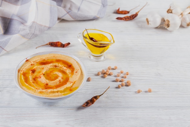Gesunder hausgemachter cremiger Hummus mit Olivenöl und trockenem Paprika auf weißer Holzoberfläche. Gesundes und diätetisches Nahrungsmittelkonzept.