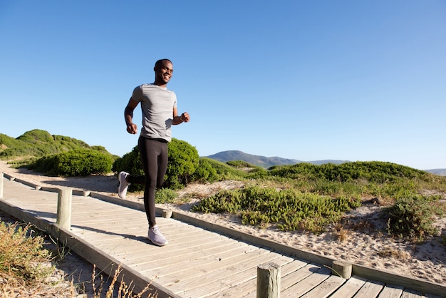 Gesunder junger afrikanischer Mann, der auf Promenade auf den Strand läuft