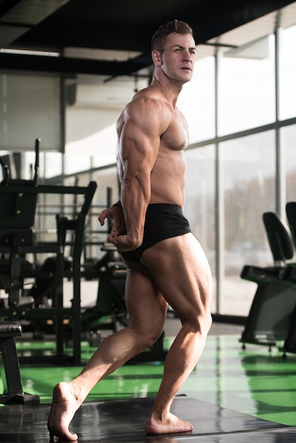 Gesunder junger Mann, der stark in der Turnhalle steht und Muskeln muskulöser athletischer Bodybuilder-Eignungs-Modell aufwirft, das nach Übungen aufwirft