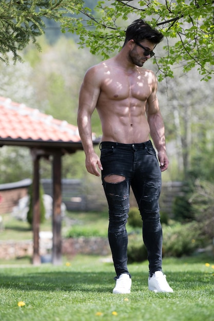Gesunder junger Mann, der stark steht und Muskeln beugt, während er schwarze Jeans trägt