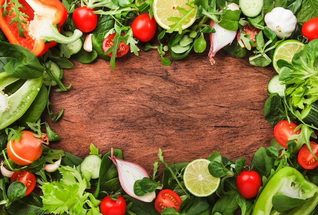 Gesunder Lebensmittelhintergrund mit verschiedenen grünen Kräutern und Gemüse Zutaten zum Kochen von Salat Vegetarisches und veganes Lebensmittelkonzept Draufsicht Holzrahmen mit Kopierraum