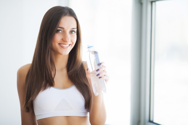 Gesunder Lebensstil. Junge Frau des schönen Sitzes, die eine Flasche Wasser hält