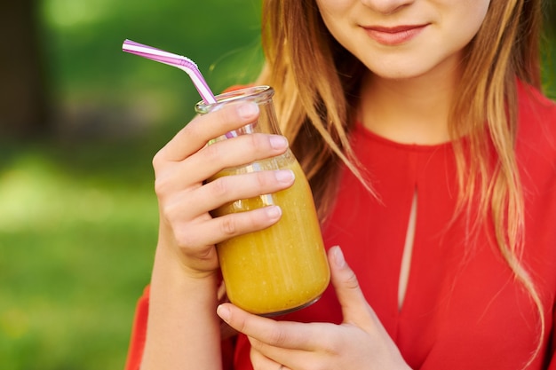 Gesunder Lebensstil. Nicht erkennbare junge Frau mit gelbem Beeren-Detox-Smoothie im Sommer, auf grünem Naturhintergrund.