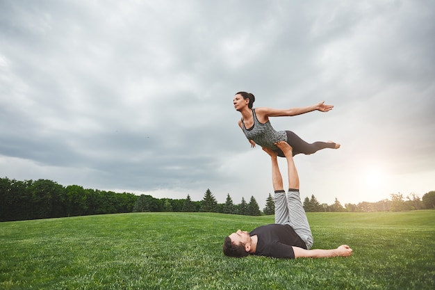 Gesunder Lebensstil starker Mann, der auf Gras liegt und Frau auf seinen Füßen balanciert junges Paar