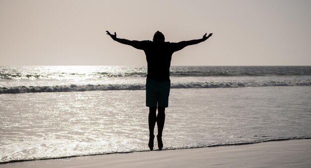 Gesunder Mann Silhouette hob die Hände am Strand energisch Sommer fühlen sich Freiheit jung und frei Sport Athlet springen in den Ozean morgendliche Trainingsaktivität