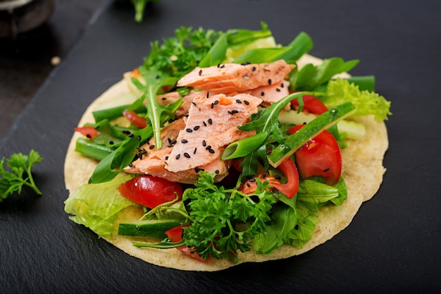 Gesunder mexikanischer Maistacos mit gebackenem Lachs, Kopfsalat, Tomate, Gurke und Arugula.