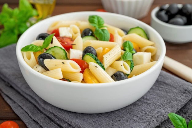 Gesunder Nudelsalat mit Tomaten, Gurken, roten Zwiebeln, Oliven und Käse in einer Schüssel Textfreiraum