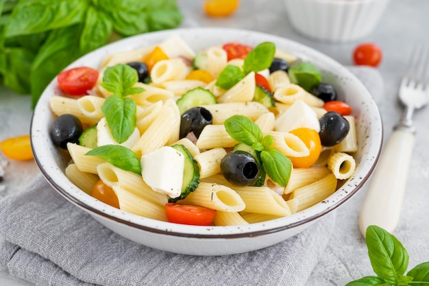 Gesunder Nudelsalat mit Tomaten Gurken roten Zwiebeln Oliven und Käse in einer Schüssel