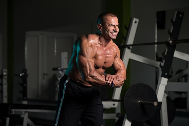 Gesunder reifer Mann, der stark in der Turnhalle steht und Muskeln muskulöser athletischer Bodybuilder-Eignungs-Mann aufwirft, der nach Übungen aufwirft