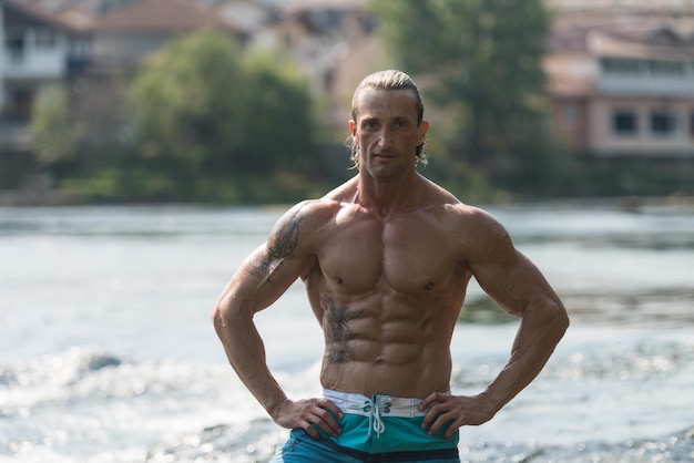 Gesunder, reifer Tattoo-Mann, der draußen in der Natur stark steht und Muskeln muskulöser, athletischer Bodybuilder-Eignungsmodell posiert, der nach Übungen posiert