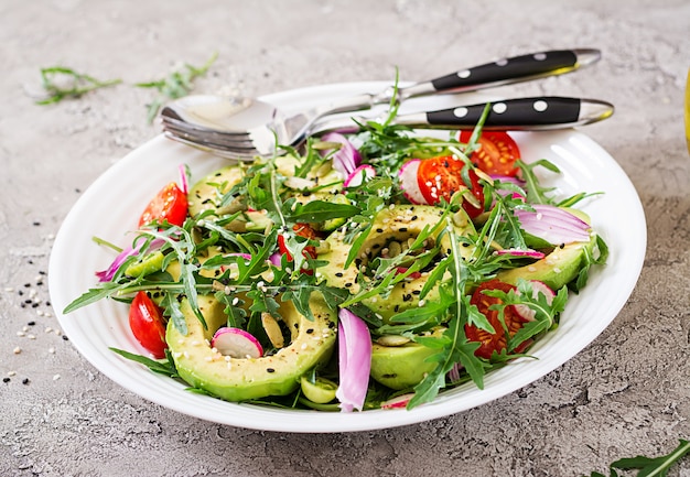 Foto gesunder salat des frischgemüses - tomaten, avocado, arugula, rettich und samen auf einer schüssel. veganes essen.