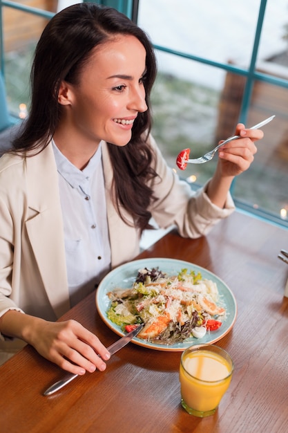 Gesunder Salat. Draufsicht der ansprechenden attraktiven aufrichtigen Frau, die Gabel beim Lächeln und beim Essen des Salats verwendet