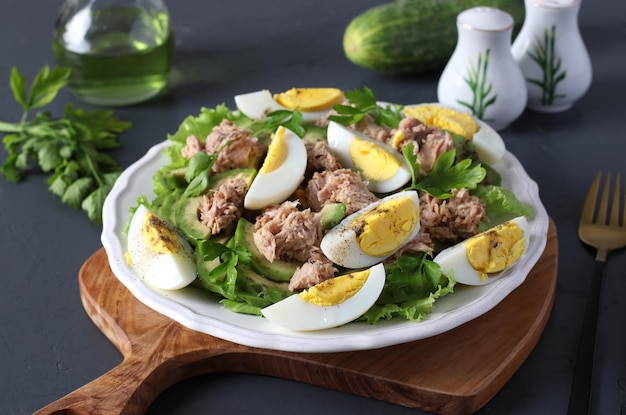 Gesunder Salat mit Avocado-Thunfisch-Eiern und Gurken auf einem weißen Teller auf einem Holzbrett