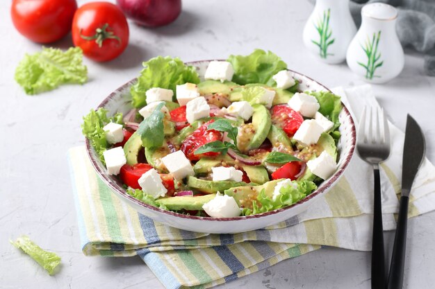 Gesunder Salat mit Avocado, Tomaten, Feta und roten Zwiebeln auf grauem Hintergrund, Tag der gesunden Ernährung