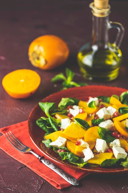 Gesunder Salat mit Kaki-Doucette, Feldsalat, Feldsalat und Feta-Käse auf einem roten Teller auf rotem Hintergrund. Superfoods Vitamin Herbst- oder Winter-Kakisalat