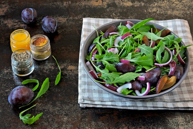Gesunder Salat mit Rucola, Pflaume und blauen Zwiebeln in einer Schüssel auf einem stilvollen schäbigen Hintergrund