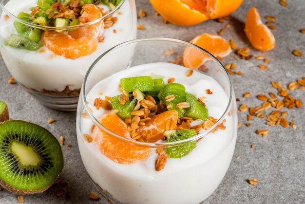 Gesunder Tangerine- und Kiwijoghurt-Granola-Nachtisch zum Frühstück, mit Bestandteilen, graue Steintabelle, nahe Ansicht