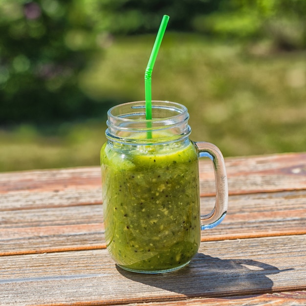 Gesunder veganer grüner Smoothie in Gläsern über Naturhintergrund.